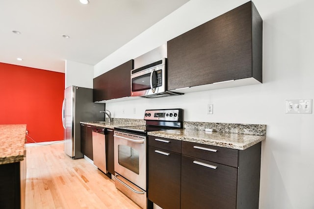 kitchen featuring dark brown cabinets, light wood-type flooring, stainless steel appliances, and light stone counters