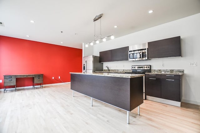 kitchen with a center island with sink, light wood-type flooring, decorative light fixtures, and appliances with stainless steel finishes