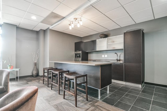 kitchen with kitchen peninsula, a paneled ceiling, dark tile patterned floors, sink, and a breakfast bar area