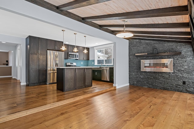 kitchen featuring appliances with stainless steel finishes, backsplash, hanging light fixtures, a center island, and dark brown cabinetry