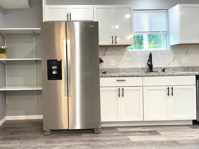 kitchen featuring white cabinetry, sink, light stone counters, stainless steel refrigerator with ice dispenser, and light hardwood / wood-style floors