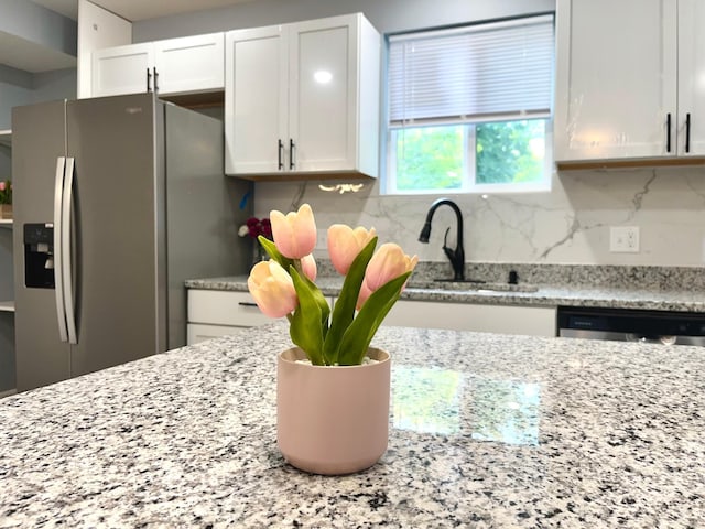 kitchen with decorative backsplash, appliances with stainless steel finishes, light stone countertops, sink, and white cabinetry