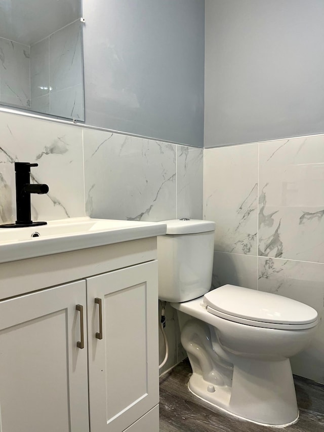 bathroom with vanity, toilet, wood-type flooring, and tile walls