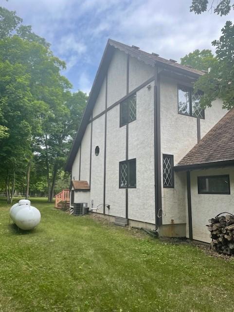 33820 County Highway 34, Sugar Bush E Twp, MN 56569 - view of side of property featuring stucco siding, a yard, a shingled roof, and central AC unit