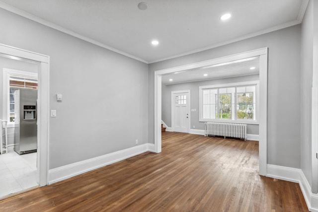 unfurnished living room with hardwood / wood-style floors, radiator, and crown molding