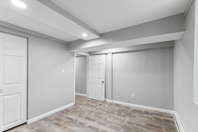 basement featuring a baseboard radiator and light hardwood / wood-style floors