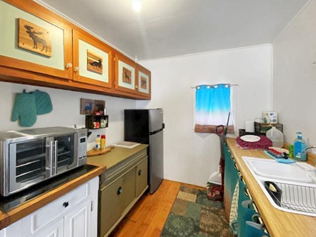 kitchen with black refrigerator, white cabinets, light hardwood / wood-style floors, and sink