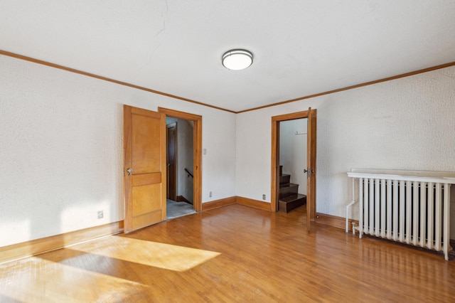 spare room with crown molding, radiator heating unit, and wood-type flooring