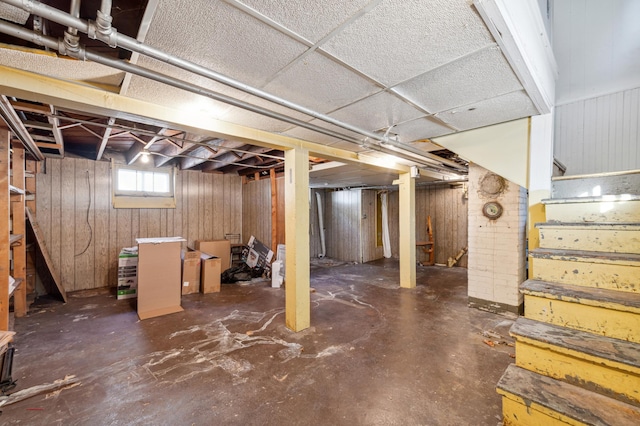 basement featuring a drop ceiling and wooden walls