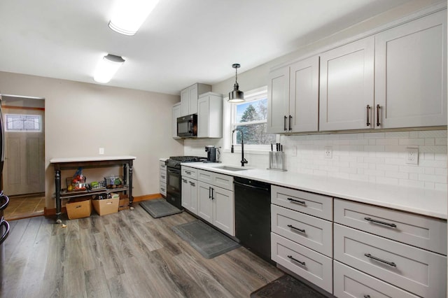 kitchen featuring backsplash, sink, black appliances, decorative light fixtures, and hardwood / wood-style floors