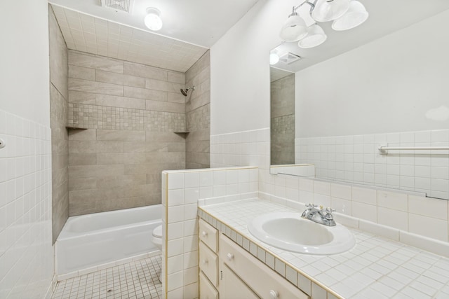 full bathroom with vanity, tile patterned floors, tiled shower / bath combo, toilet, and tile walls