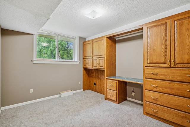 unfurnished office with built in desk, a textured ceiling, and light carpet