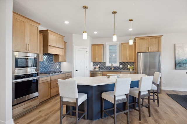 kitchen with appliances with stainless steel finishes, backsplash, light wood-type flooring, hanging light fixtures, and a center island