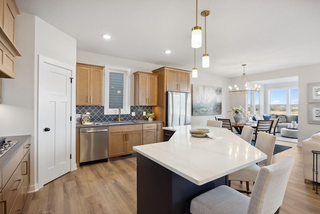 kitchen with an inviting chandelier, appliances with stainless steel finishes, a kitchen island, pendant lighting, and sink