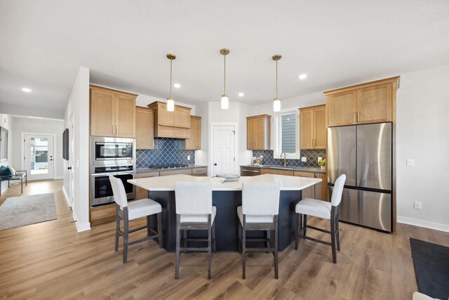 kitchen with a kitchen bar, appliances with stainless steel finishes, light wood-type flooring, hanging light fixtures, and a kitchen island