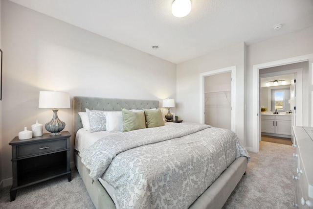 bedroom with light colored carpet, a closet, a walk in closet, and connected bathroom