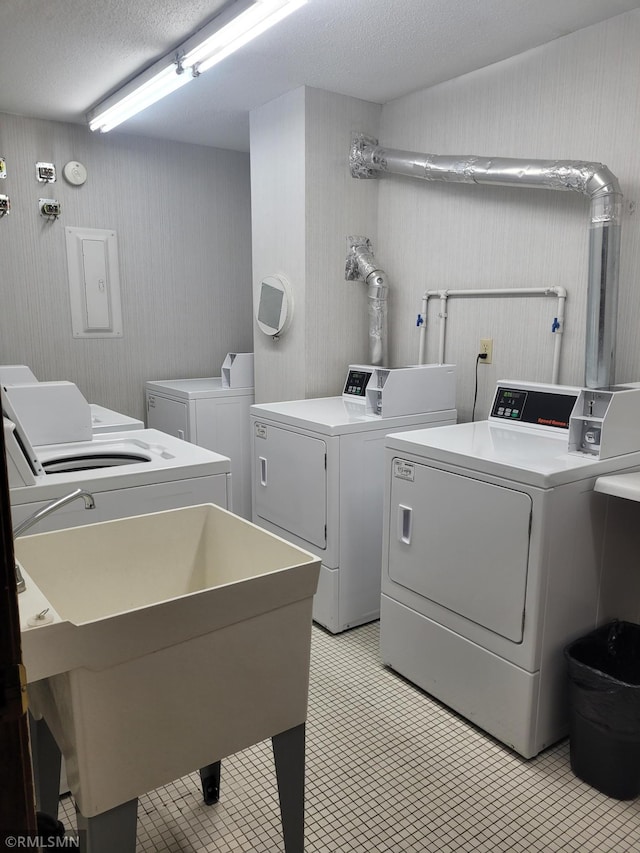 washroom featuring washer and dryer, a textured ceiling, electric panel, and sink