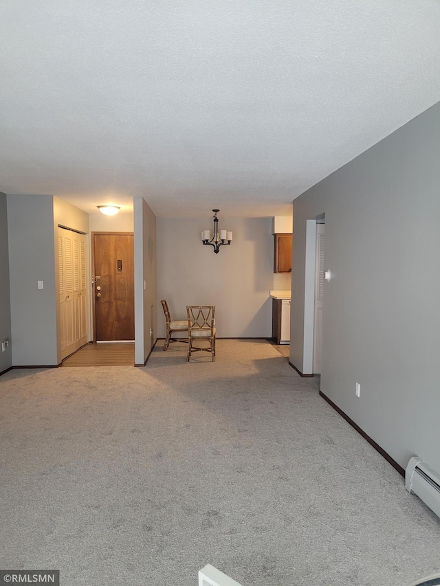 spare room with baseboard heating, light colored carpet, and an inviting chandelier