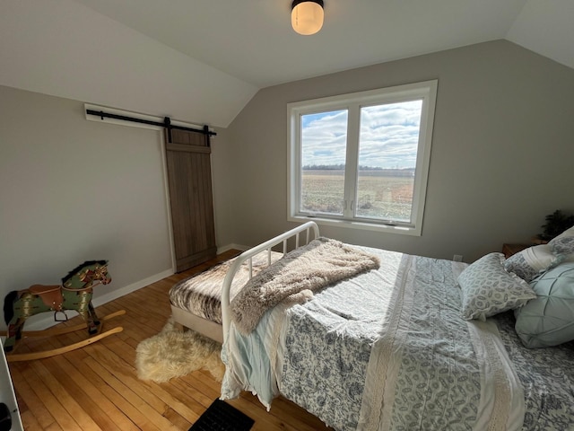 bedroom with a barn door, hardwood / wood-style floors, and vaulted ceiling