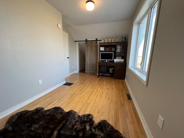 office with a barn door, light hardwood / wood-style flooring, and vaulted ceiling