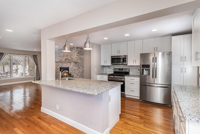 kitchen featuring appliances with stainless steel finishes, sink, a wood stove, light hardwood / wood-style flooring, and white cabinetry