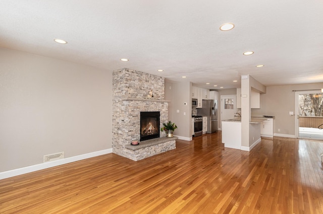 unfurnished living room featuring a textured ceiling, a stone fireplace, light wood-type flooring, and sink