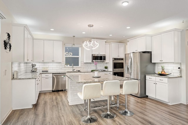 kitchen featuring stainless steel appliances, light stone countertops, white cabinets, a kitchen island, and decorative light fixtures