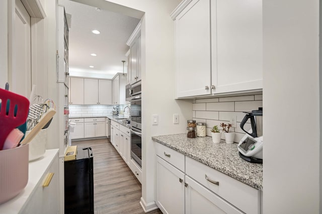 kitchen featuring white cabinetry, light stone countertops, light hardwood / wood-style flooring, and decorative backsplash