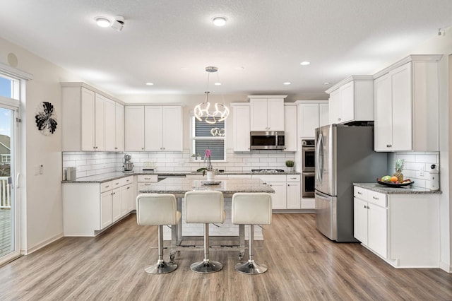 kitchen with light stone counters, decorative light fixtures, white cabinetry, and appliances with stainless steel finishes