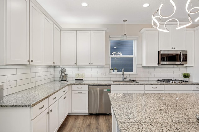 kitchen with sink, appliances with stainless steel finishes, white cabinetry, light stone counters, and decorative light fixtures