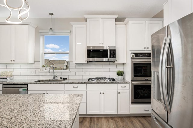 kitchen with sink, white cabinetry, appliances with stainless steel finishes, pendant lighting, and light stone countertops