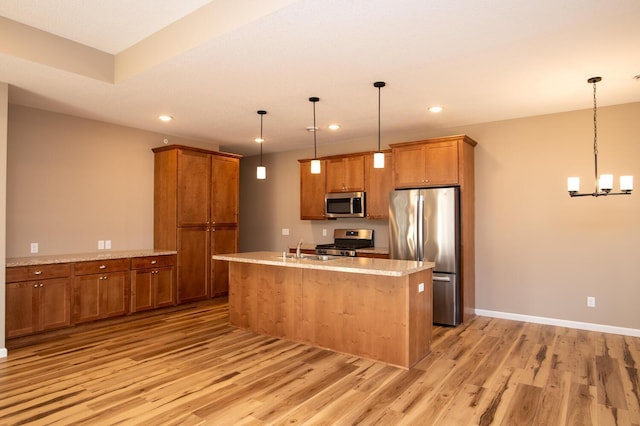 kitchen featuring appliances with stainless steel finishes, sink, light hardwood / wood-style floors, hanging light fixtures, and an island with sink