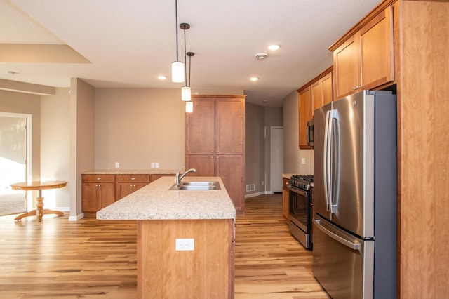 kitchen with sink, stainless steel appliances, an island with sink, pendant lighting, and light wood-type flooring