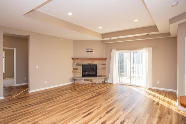 unfurnished living room with a tray ceiling, a stone fireplace, and light hardwood / wood-style flooring