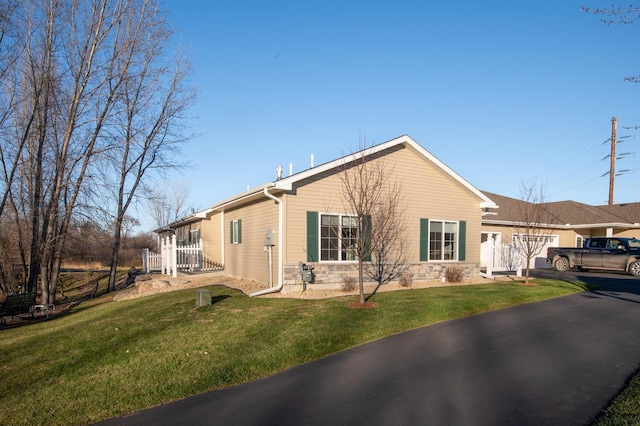 view of front facade featuring a front lawn, fence, aphalt driveway, a garage, and stone siding