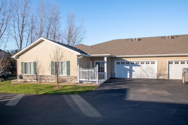 single story home featuring aphalt driveway, stone siding, a garage, and roof with shingles