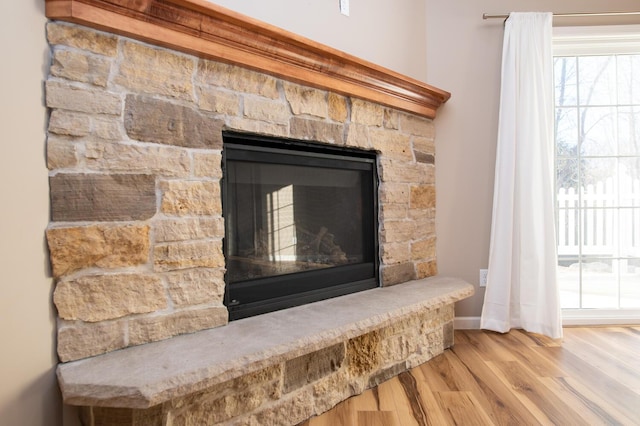 room details with baseboards, a stone fireplace, and wood finished floors