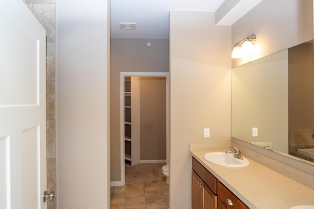 full bathroom with a walk in closet, double vanity, toilet, and a sink