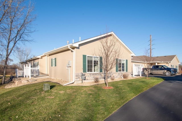 view of property exterior featuring aphalt driveway, a lawn, and stone siding