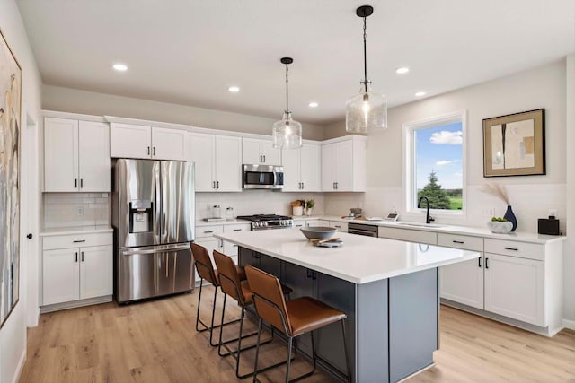 kitchen featuring white cabinets, light hardwood / wood-style floors, decorative light fixtures, a kitchen island, and stainless steel appliances