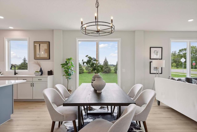 dining space with a healthy amount of sunlight, light wood-type flooring, sink, and an inviting chandelier