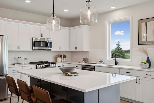 kitchen with appliances with stainless steel finishes, white cabinetry, a kitchen island, and hanging light fixtures