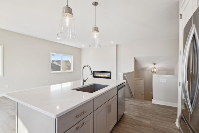 kitchen featuring sink, wood-type flooring, decorative light fixtures, an island with sink, and stainless steel appliances