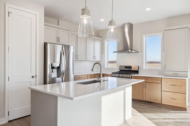 kitchen with wall chimney exhaust hood, sink, white cabinetry, an island with sink, and stainless steel appliances