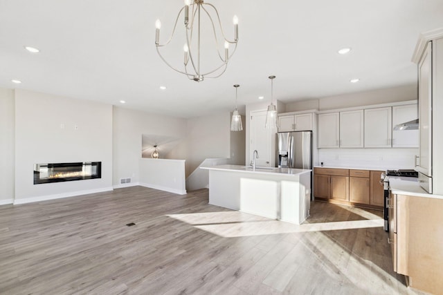 kitchen featuring pendant lighting, light wood-type flooring, stainless steel appliances, and a center island with sink