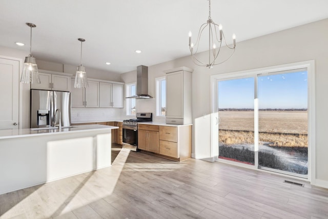 kitchen featuring wall chimney exhaust hood, stainless steel appliances, hanging light fixtures, and white cabinets