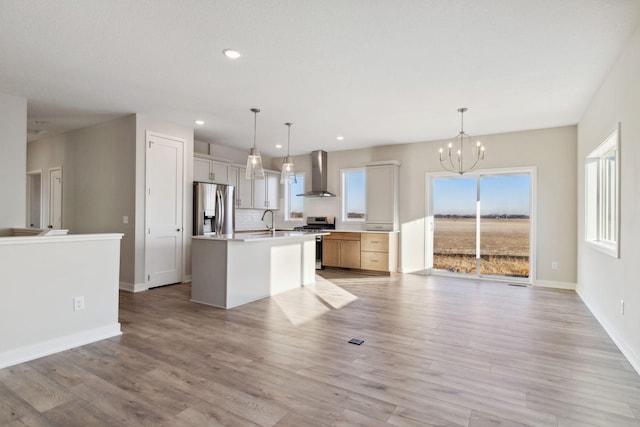 kitchen with wall chimney exhaust hood, appliances with stainless steel finishes, a kitchen island with sink, and pendant lighting