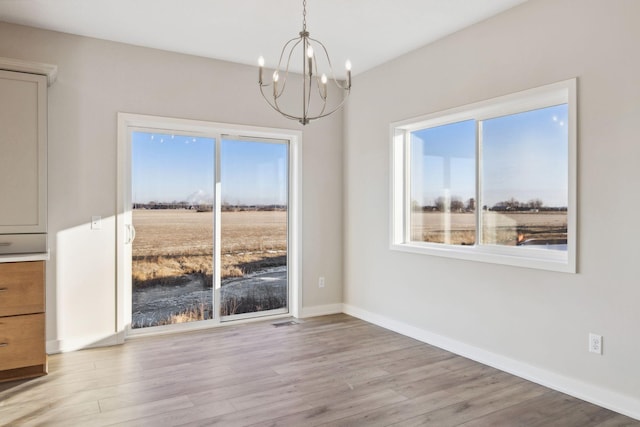 unfurnished dining area featuring an inviting chandelier and light hardwood / wood-style flooring