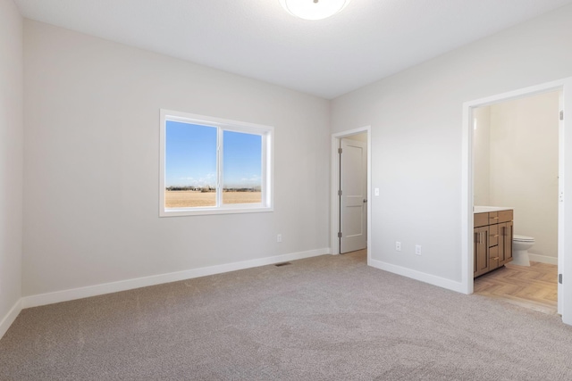 unfurnished bedroom with ensuite bathroom and light carpet