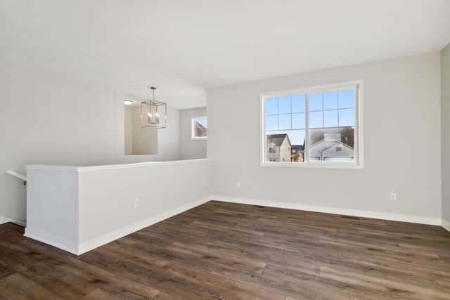 spare room featuring dark wood-type flooring and an inviting chandelier